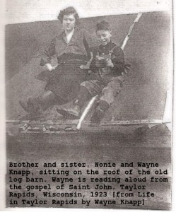 Nora and Wayne sitting on log house roof reading, circa 1923
